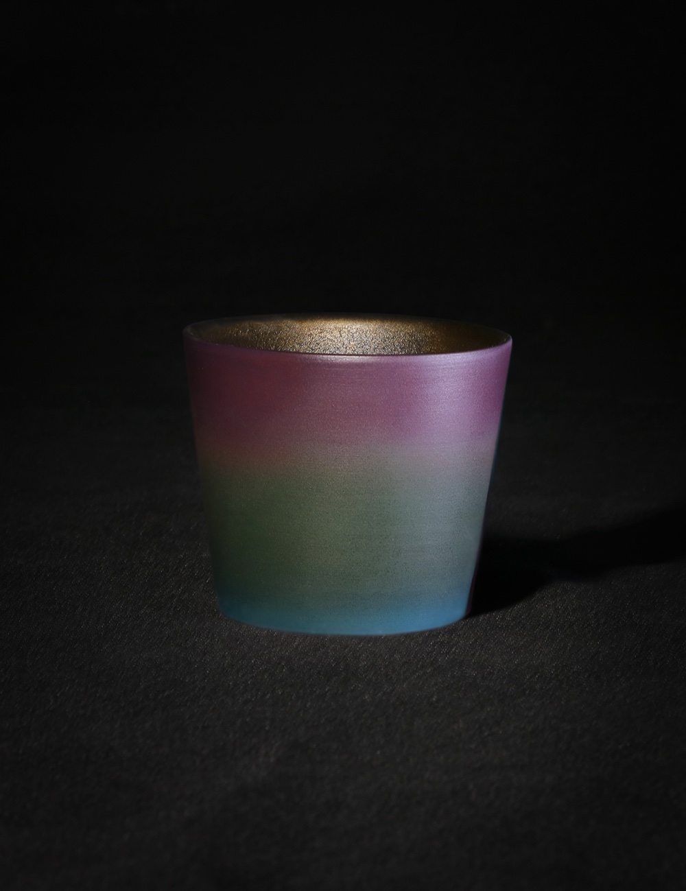 Gradient ceramic cup with pink, green and blue glaze on black background